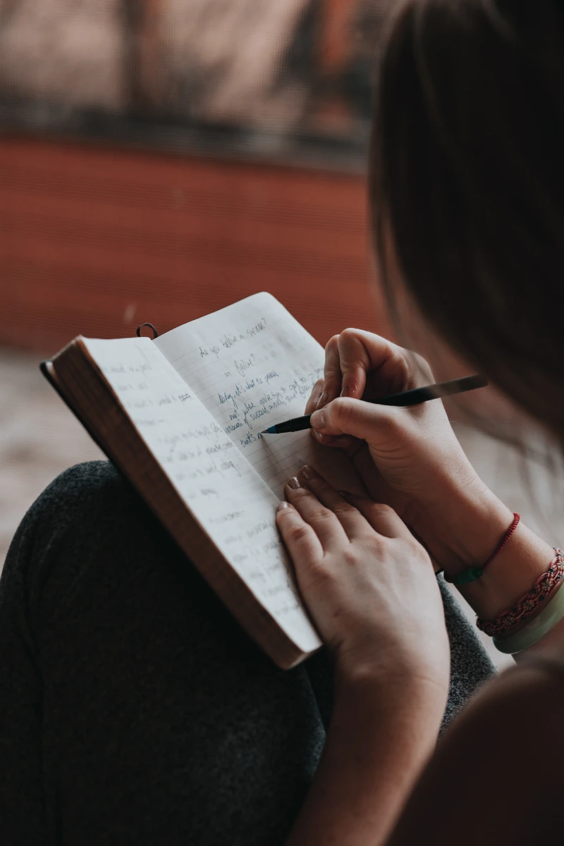 Adolescente escribiendo a mano en diario sobre sus piernas